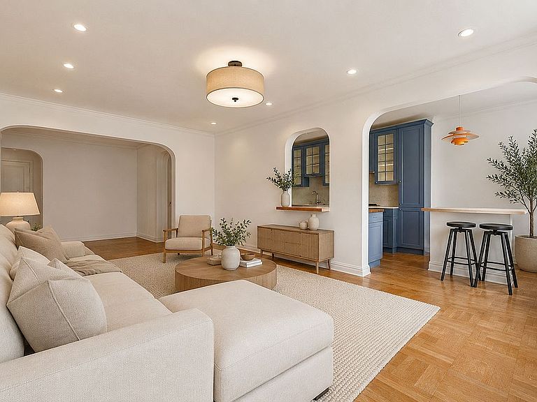 Open living and dining area of unit 3T showing the arched pass-through to the kitchen, the periwinkle blue cabinetry visible in the next room, and herringbone floors